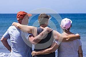 Back view of group of three friends senior people enjoying together the beach looking at the horizon over water - concept of