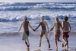 Back view of group of young people men and women run at the beach to the water - tourists and summer holiday vacation together