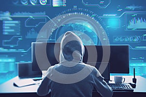 Back view of hacker in hoodie sitting at desktop with coffee cup and using computer monitors with abstract glowing digital