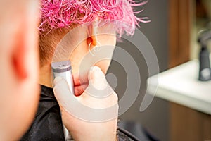 Back view of hairdresser's hand shaving nape and neck with electric trimmer of young caucasian woman with short pink