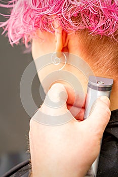 Back view of hairdresser& x27;s hand shaving nape and neck with electric trimmer of young caucasian woman with short pink