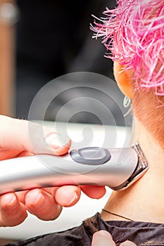 Back view of hairdresser& x27;s hand shaving nape and neck with electric trimmer of young caucasian woman with short pink