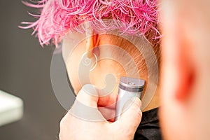 Back view of hairdresser& x27;s hand shaving nape and neck with electric trimmer of young caucasian woman with short pink