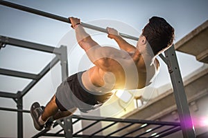 Back view of handsome shirtless man exercising on horizontal bar outdoors. Calisthenics workout.