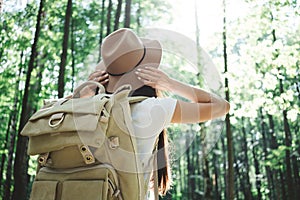 Back view on handsome traveler hipster girl with backpack and hat walking in forest among trees