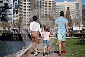 Back view of happy american parents holding hands with son and walking in sunny summer citi street, tender family moment