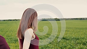 A back view of a happy cuple walking in a field. A beautiful young woman taking her man by the hand.