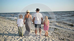 Back View of Happy Family Looking on the Sea During Summer Vacation. Mother, Father, Son and Daughter Holding Hands on