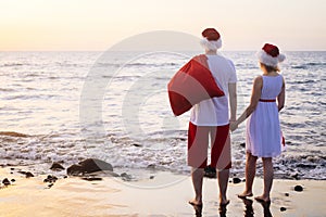 back view Happy family in Santa Claus hats celebrating Christmas on beach. people traveling to warm countries on winter