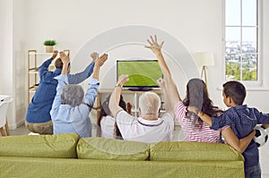 Back view of happy family sitting on sofa at home and watching football match on TV