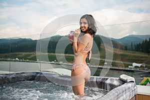 Back view of happy girl in bikini standing with cocktail at the Jacuzzi outdoors on vacation