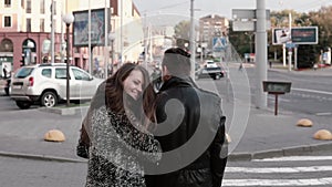 Back view of happy lovers walking in the street. Beautiful girl looks back into camera smiling. Slow mo, steadicam shot