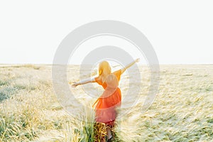 Back view happy woman with raised arms relaxing in wheat field on sunset. Celebrating freedom. Positive emotion, feeling