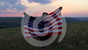 Back view happy woman standing with her back on sunset in nature iwith open hands with USA flag