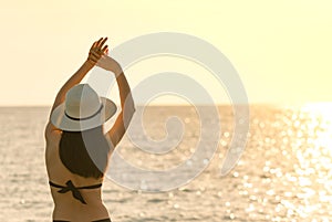 Back view of happy young Asian woman in black swimsuit and straw hat relax and enjoy holiday at tropical paradise beach at sunset