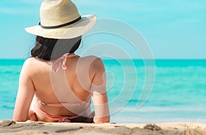 Back view of happy young Asian woman in pink swimsuit and straw hat relax and enjoy holiday at tropical paradise beach at sunset.