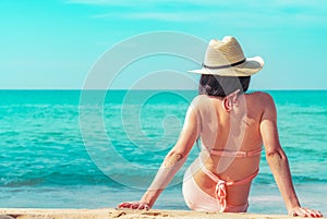 Back view of happy young Asian woman in pink swimsuit and straw hat relax and enjoy holiday at tropical paradise beach at sunset.