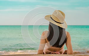 Back view of happy young Asian woman in pink swimsuit and straw hat relax and enjoy holiday at tropical paradise beach at sunset.