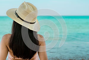 Back view of happy young Asian woman in pink swimsuit and straw hat relax and enjoy holiday at tropical paradise beach at sunset.