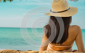 Back view of happy young Asian woman in pink swimsuit and straw hat relax and enjoy holiday at tropical paradise beach at sunset.