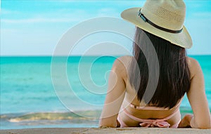 Back view of happy young Asian woman in pink swimsuit and straw hat relax and enjoy holiday at tropical paradise beach at sunset.