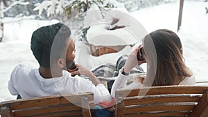 Back view. Happy young couple drinking hot chocolate while sitting on the bench outdoors on Valentines day