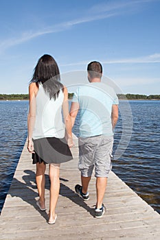 Back view of happy young couple in love in pontoon bridge on lake