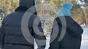 Back view happy young couple strolling in slow motion in winter forest holding hands. Relaxed carefree Caucasian man and