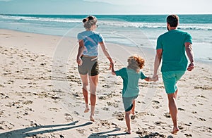 Back view of happy young family walking on sand beach. Child with parents holding hands. Full length poeple.