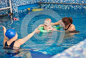 Happy mother and her son laughing baby boy having fun during swimming exercising with trainer in paddling swimming pool