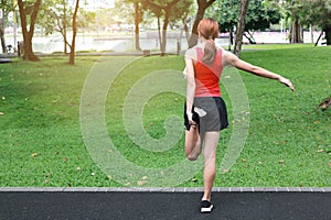 Back view of healthy Asian woman stretching her legs before run in park. Fitness and exercise concept.