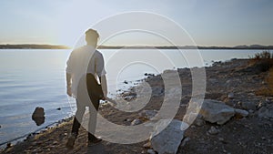 Back view of a hipster man walking along the beach against the sun holding a guitar, Torrevieja Pink lake in Alicante