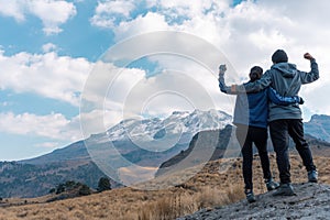 A back view of a Hispanic couple admiring the Iztaccihuatl volcanic mountain doing a winner gesture photo