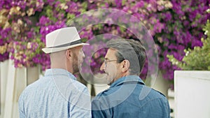 Back view of homosexual men going to garden with lilac trees