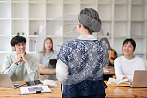 A back view image of a teacher professor giving a lecture to her students in the classroom