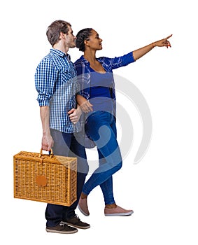 Back view of interracial going couple with a picnic bag who points somewhere
