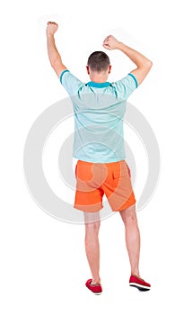 Back view of joyful man celebrating victory hands up.