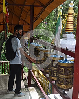 Back view of a Ladakhi young guy wearing face mask with turning Buddhist prayer wheel in Tso-Pema