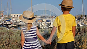 Back view of the little boy and girl holding hands on the quay of the yacht port