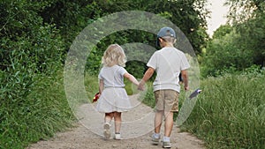 Back view little boy and girl holding hands are walking outdoors