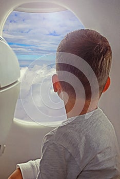 Back view of little boy looking aerial view of sky and cloud outside airplane window