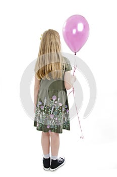 Back view of little girl looking at wall holding pink balloon. Rear view.