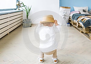 Back view on a little girl in a straw hat. The baby girl plays in the light room, indoors