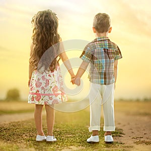 Back view of little kids holding hands at sunset