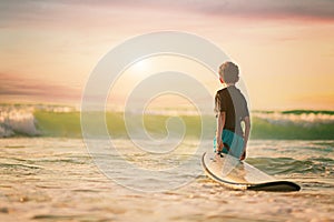 Back view of the little surfer boy surfing lifestyle relaxing holding surfboard looking at ocean waves for surf