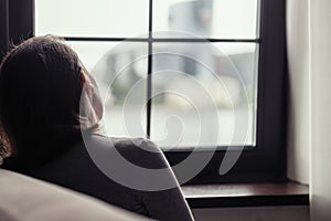 Back view of lonely sad young brunette woman sitting near window. Concept.