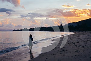 Back view of lonely woman walking on beach in sunset