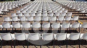 Back view of long rows of empty white plastic chairs geometrically arranged under the sun.