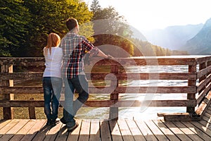 Back view of lovely couple Posing. On the background a beautiful sunset on the lake. Rest and vacation in nature. Wooden pier.