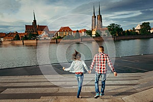 Back view of the loving couple holding hands and jumping down the stairs in the front of Ostrow Tumski in Poland.